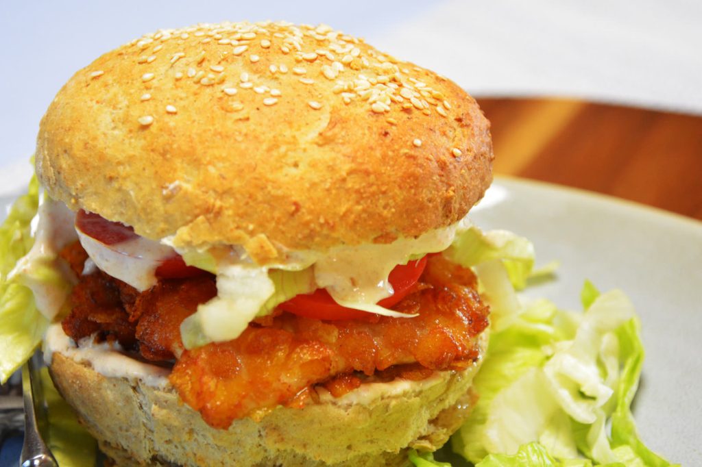 Burger z kurczakiem w chrupiącej panierce z płatków kukurydzianych, z pomidorem, sałatą i sosem chili w bułce z sezamem