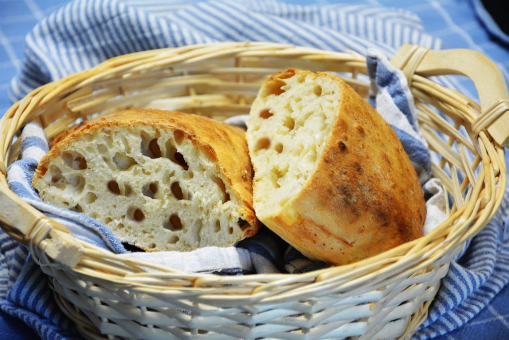 Domowa ciabatta z chrupiącą, ciemną skórką, przekrojona tak, że widać puszysty miąższ z dużymi dziurami