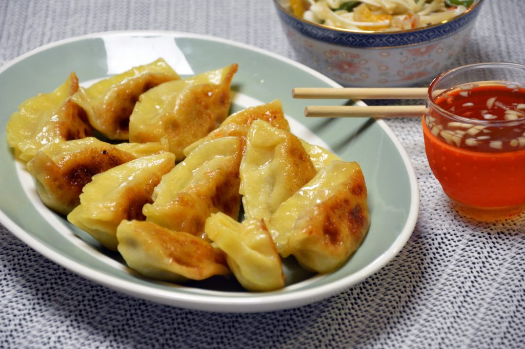 Domowe pierożki gyoza z chrupiącym spodem usmażone na patelni, podane z sosem