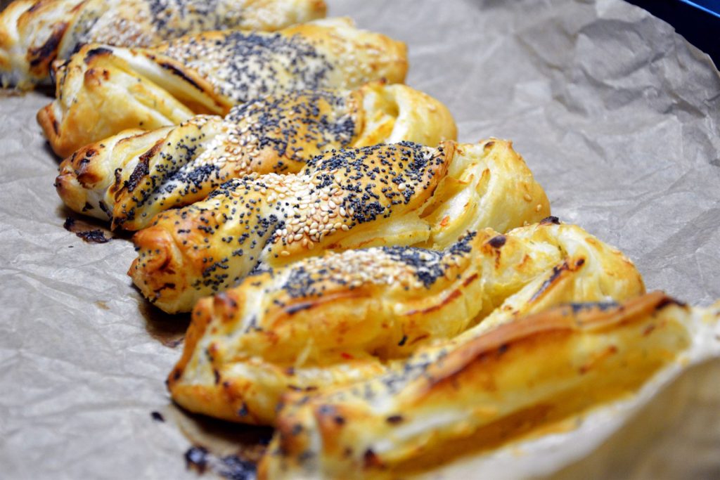 Świeżo upieczone skręcane paluchy z ciasta francuskiego z niebieskim makiem i sezamem na papierze do pieczenia