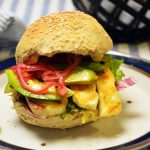 Burger w bułce sezamowej z grillowanymi plastrami halloumi, awokado, marynowaną czerwoną cebulą i sałatą na talerzu