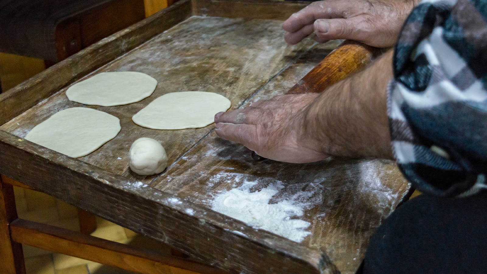 Rozwałkowane ciasto na pierogi z wyciętymi kółkami i szklanką na drewnianym blacie posypanym mąką