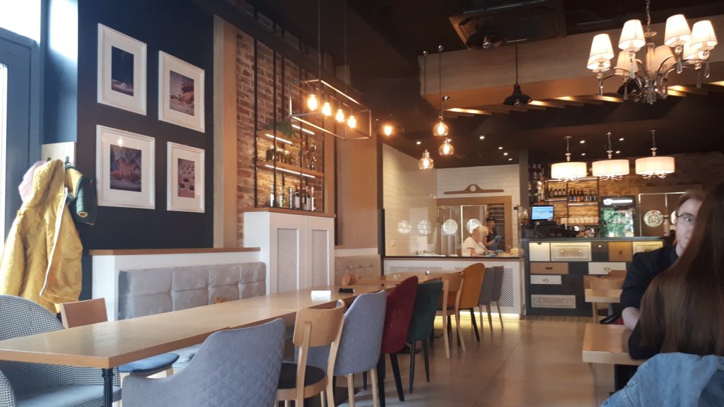Wnętrze nowoczesnej restauracji ze stolikami, krzesłami w kolorach i barem w tle