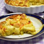 Kawałek tarty z brokułami, porem i groszkiem na talerzu, a za nim złocista tarta w formie